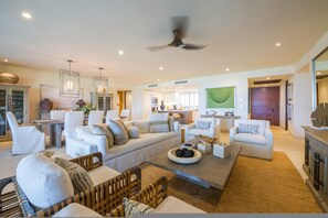 A spacious living room with a large sofa set, a coffee table, and a dining area with a kitchen in the background. - Condo Ginger 3BD - Tau Punta Mita (Punta de Mita)