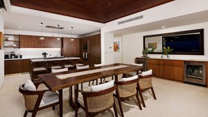 A modern kitchen with wooden cabinets, a central island, and a dining area with wicker chairs. - PH Prima Vista 4BD - Tau Punta Mita (Punta de Mita)