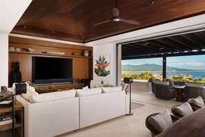 Ein modernes Wohnzimmer mit einem großen Flachbildfernseher, einer Couch und Blick auf den Ozean.