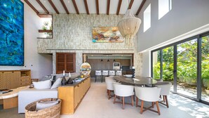 A spacious living area with a high ceiling, a large painting, and a dining area with modern chairs and a bar. - Mataiza 5BD - Iyari Punta Mita (Punta de Mita)