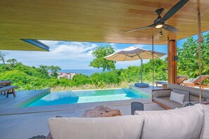 Ein Poolbereich mit Blick auf den Ozean, einem Deckenventilator und Gartenmöbeln.