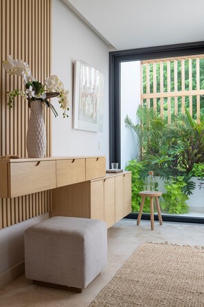 A modern interior with a wooden cabinet, a vase with white flowers, a small stool, and a view of greenery outside. - Casa Todos Juntos 8BD - Bolongo Punta Mita (Punta de Mita)