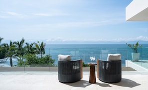 A balcony with two chairs and a small table, overlooking a coastal view with palm trees and the sea. - Casa Todos Juntos 8BD - Bolongo Punta Mita (Punta de Mita)