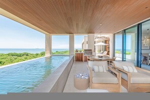 Ein moderner Infinity-Pool mit Blick auf das Meer, ein Essbereich mit Gartenmöbeln und eine Küche mit Grill.