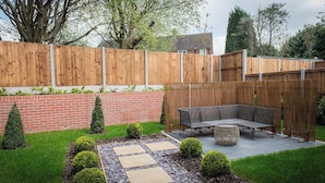 A backyard with a wooden fence, a brick wall, a patio with a table and chairs, and a garden with trimmed bushes. - House - Sleeps 6 - Parking - Garden (Newcastle)