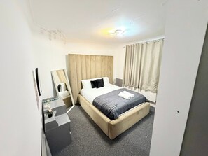 A hotel room with a bed, a bedside table, a mirror, and a window with curtains. - 7 Guests 3-Br free parking-near Manchester Airport (Cheadle)
