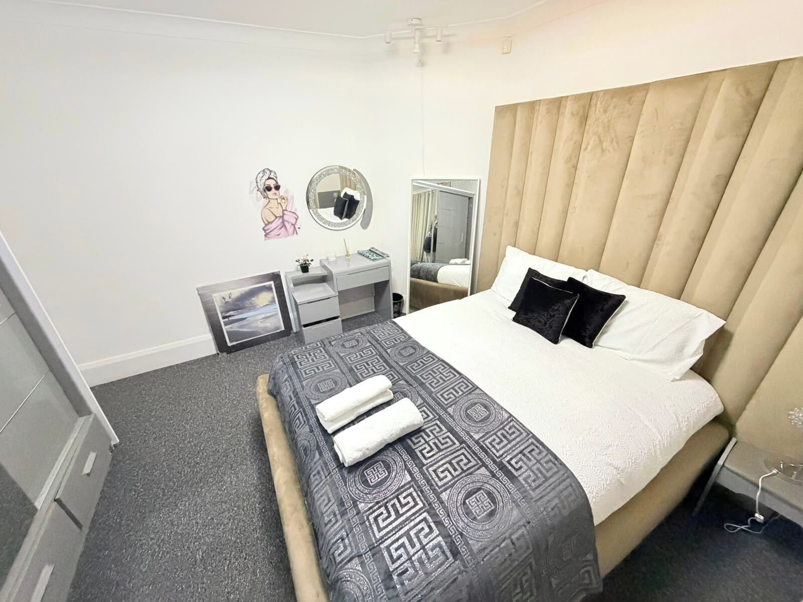 A hotel room with a bed, a bedside table, a mirror, a wardrobe, and a wall decoration.