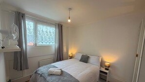 Une chambre à coucher avec un lit, des lampes de chevet, une fenêtre avec des rideaux, un radiateur et un ventilateur de plafond.