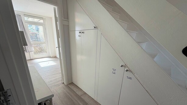Un couloir doté d’un plancher en bois menant à une porte avec un panneau de verre.
