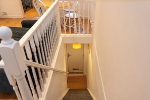 Eine Treppe mit weißen Spindeln, die zu einer Zwischenebene mit einer Tür und einer Leuchte führt.