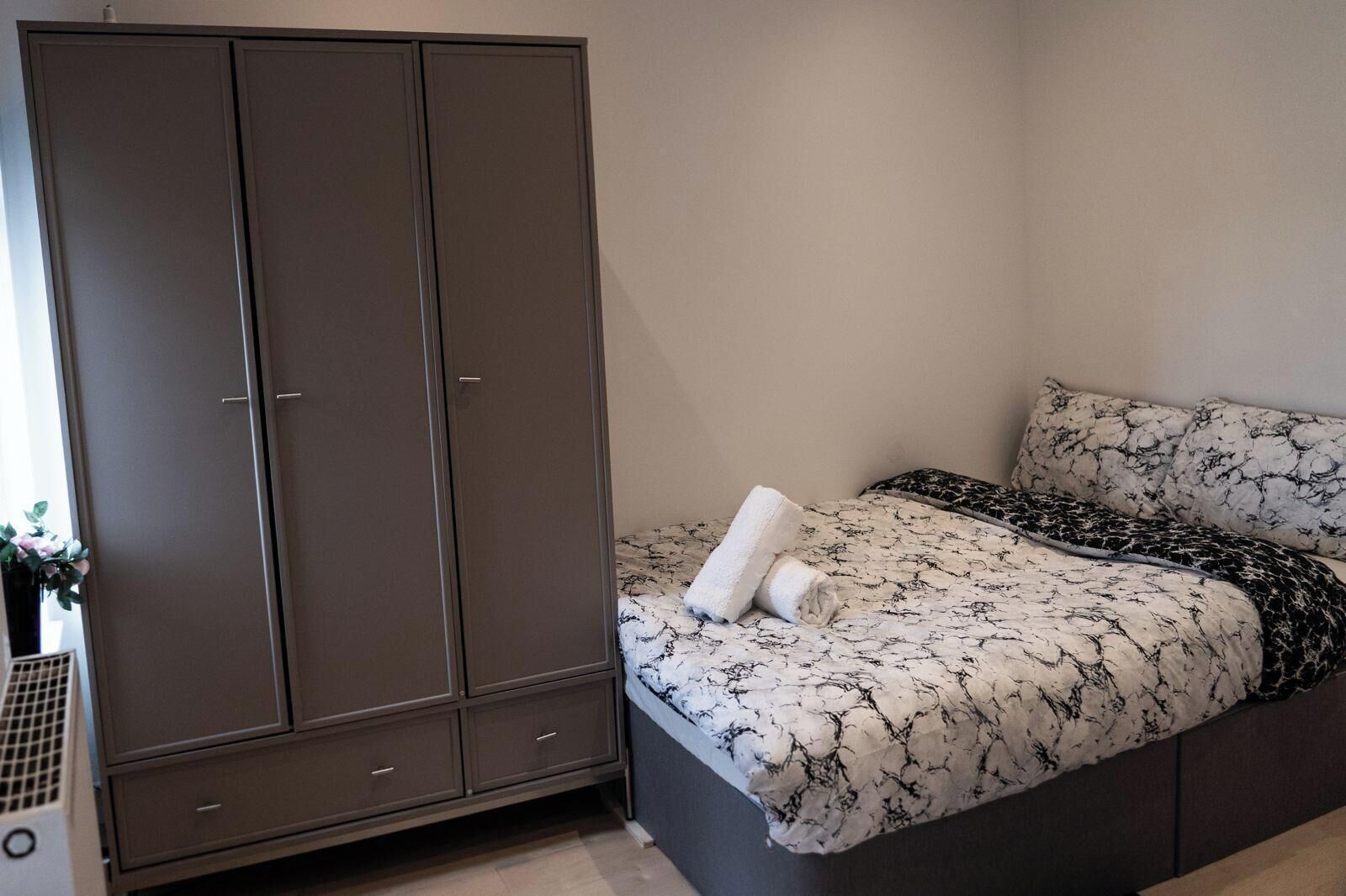A bedroom with a bed, a wardrobe, and a small plant.