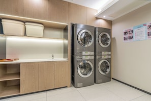 Lavandería con dos lavadoras de carga frontal apiladas, un mostrador con lavabo y armarios de madera.