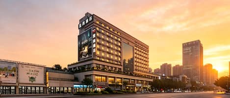 A multi-story hotel with a modern facade, located in an urban setting with a sunset in the background.