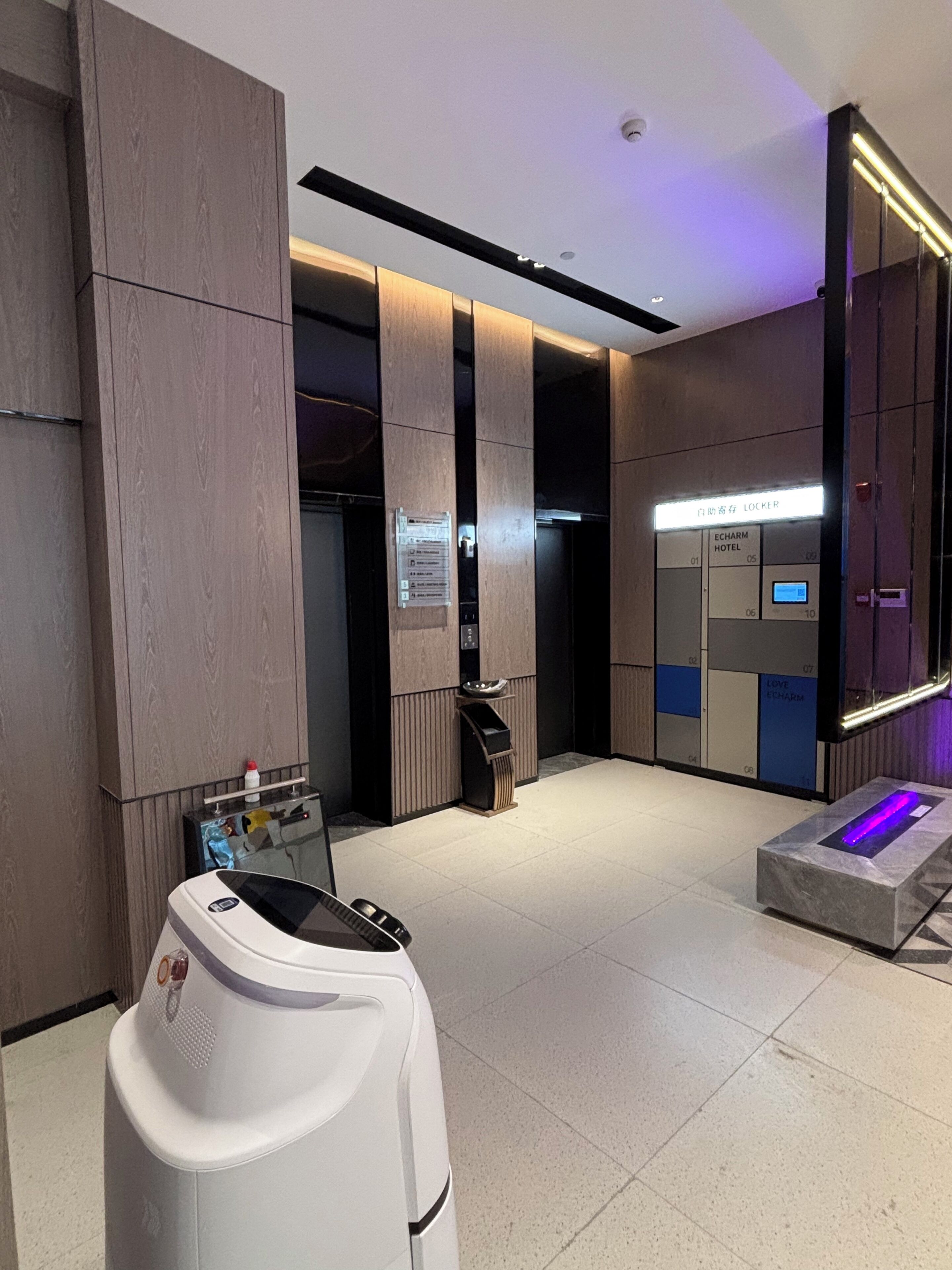 Un espace moderne pour les ascenseurs, doté d’un écran numérique, d’une poubelle et d’un distributeur d’eau.