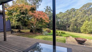 A deck with a glass table, surrounded by a garden with various plants and trees. - Masked Owl Retreat offers boutique accommodation nestled in the Otway Forest. (Forrest)