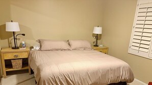 Una camera da letto con un letto, due comodini con lampade, un cestino e una finestra con persiane.