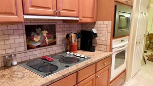 Una cucina con mobili in legno, un piano di lavoro in granito, un fornello, un forno a microonde e una macchina da caffè.