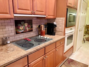 A kitchen with wooden cabinets, a granite countertop, a stove, a microwave, and a coffee maker.