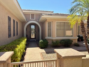 A residential building with a central entrance, a covered porch, and a small garden area with a palm tree.