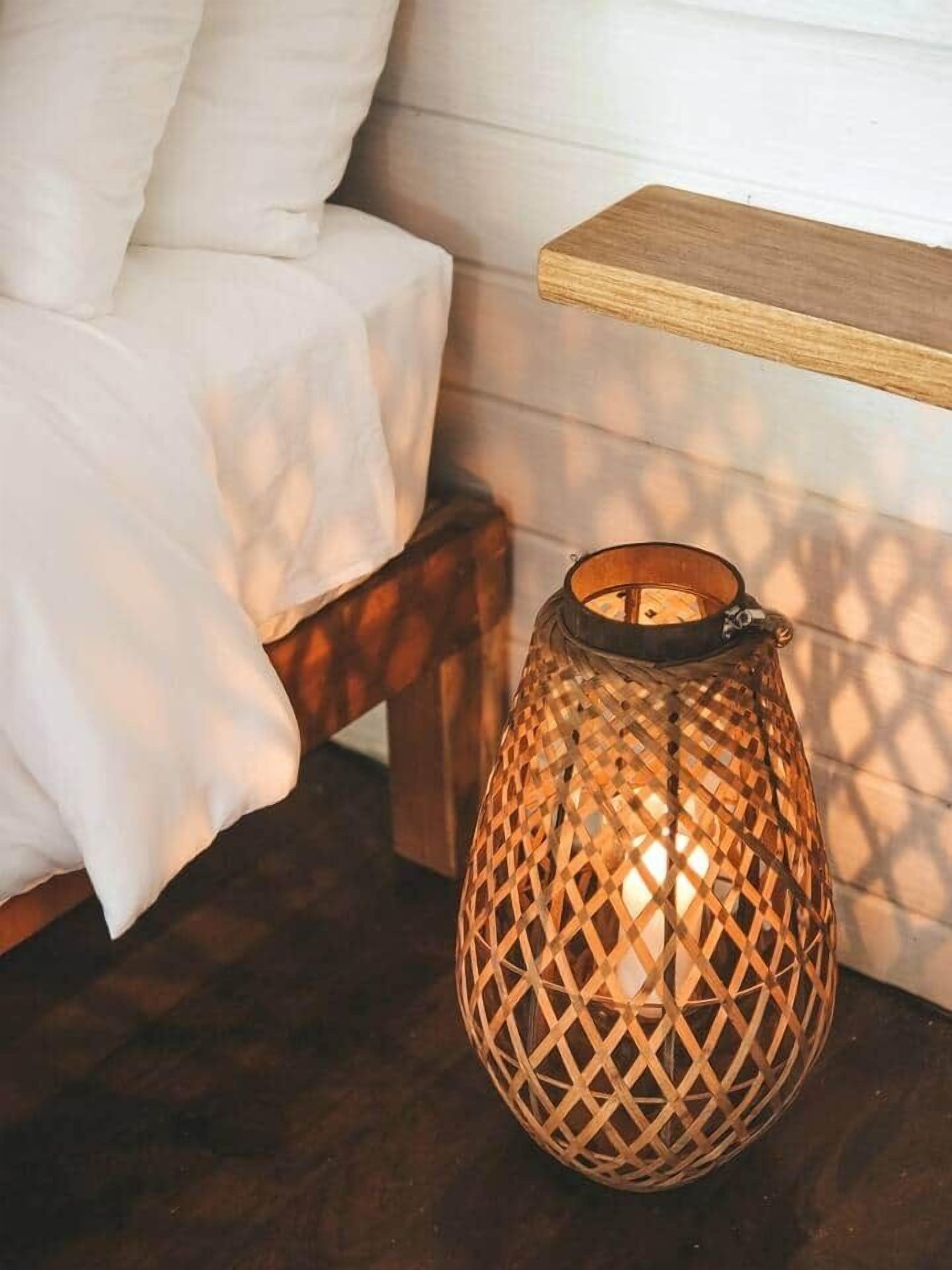 A room with a bed, a wooden shelf, and a woven lantern on a wooden floor.