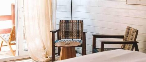Ein Hotelzimmer mit einem Bett, zwei Stühlen, einem kleinen Tisch, einer Lampe und einer Glastür, die zu einem Außenbereich führt.