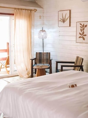 A hotel room with a bed, two chairs, a small table, a lamp, and a sliding glass door leading to an outdoor area. - Seashell suite beachfront with pool access (Saint Andrew Parish)
