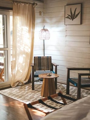 A room with a wooden floor, a patterned rug, a round table, two chairs, a hanging light fixture, and a window with a curtain. - Seashell suite beachfront with pool access (Saint Andrew Parish)