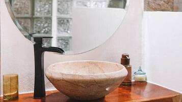 Un baño con espejo redondo, lavabo tipo cuenco y encimera de madera.