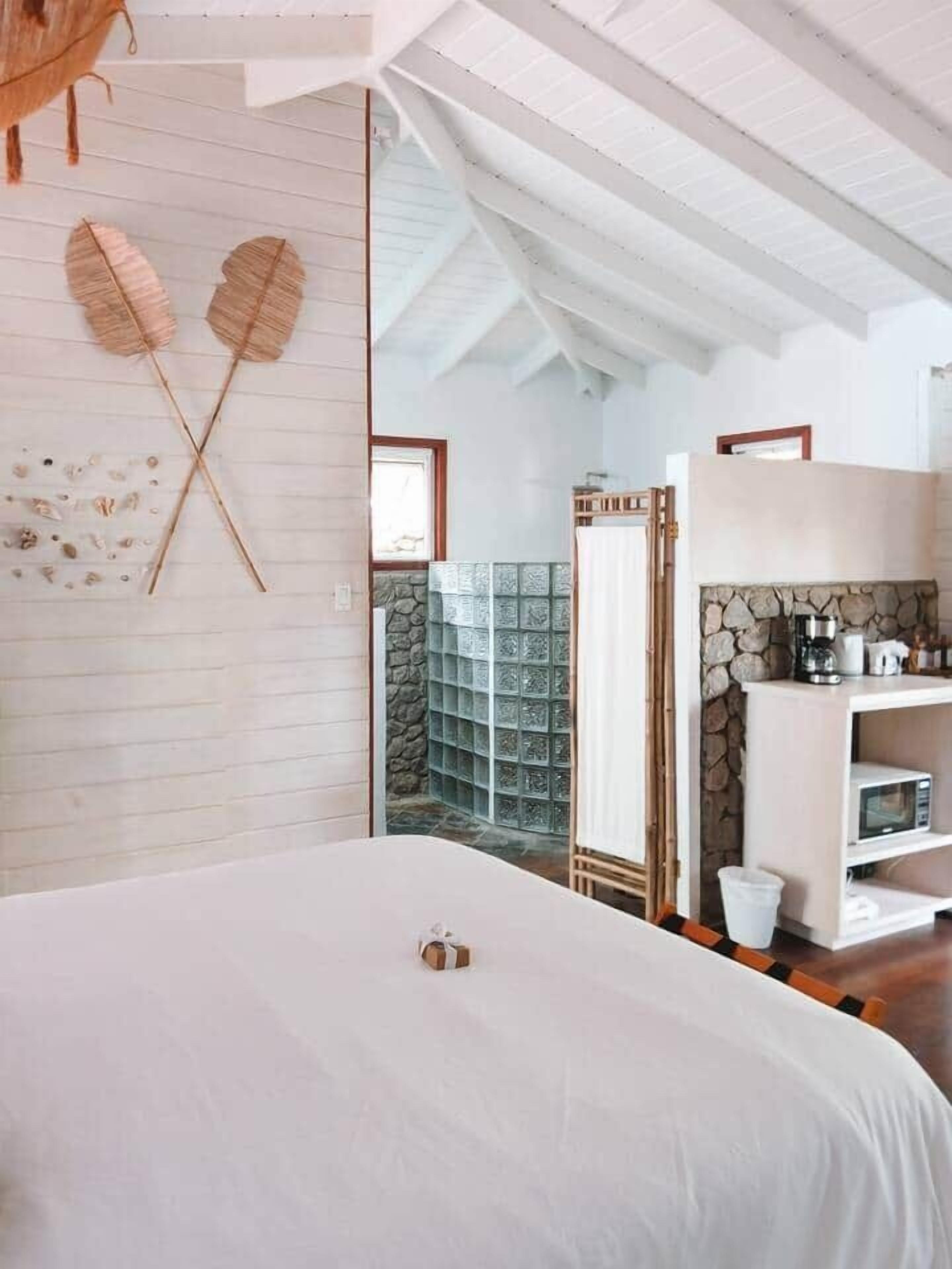 A bedroom with a large bed, a wooden wall decoration, a stone wall, and a white shelf with a kettle.