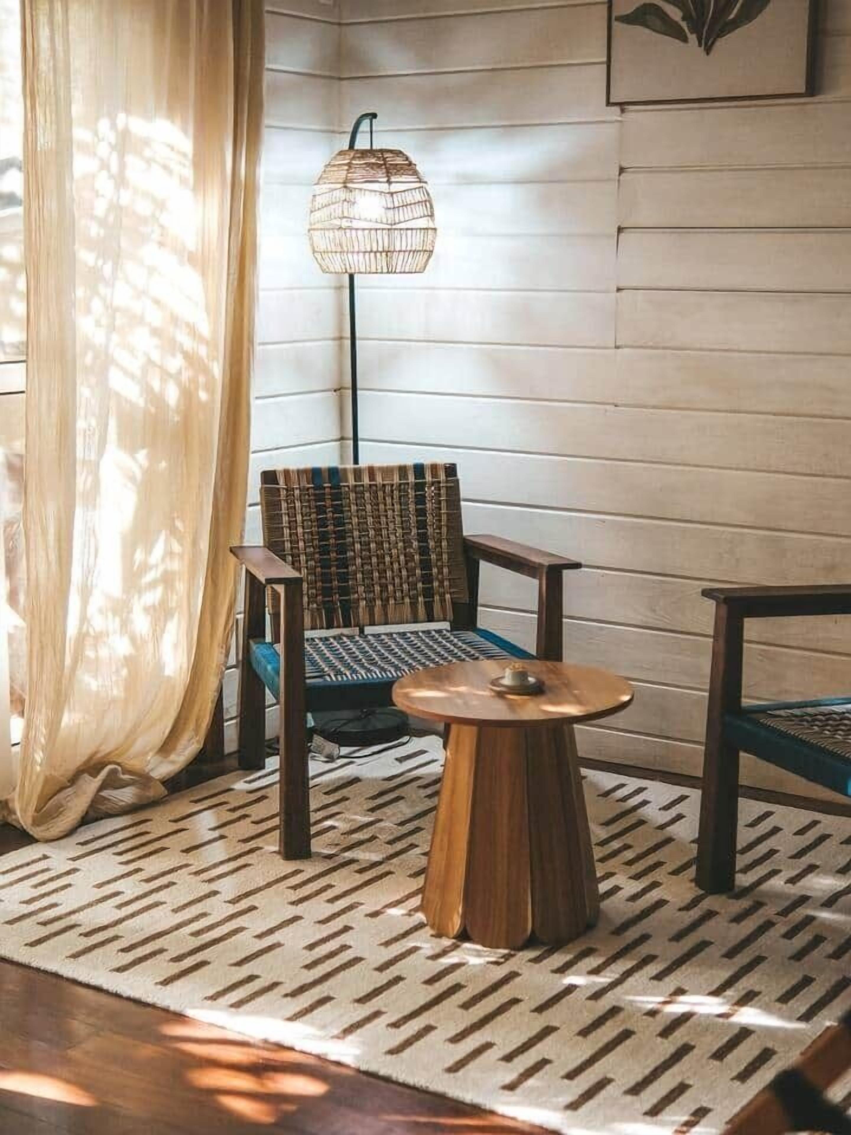 Een kamer met een vloerlamp van geweven materiaal, een kamerbreed tapijt met dessin en een stoel met een geweven zitvlak.