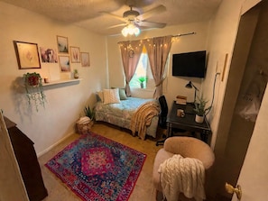Ein Schlafzimmer mit einem Bett, Schreibtisch, Stuhl und einem großen Teppich.