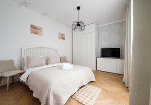 Une chambre à coucher avec un lit, une chaise, une armoire, un téléviseur et une fenêtre avec des rideaux.