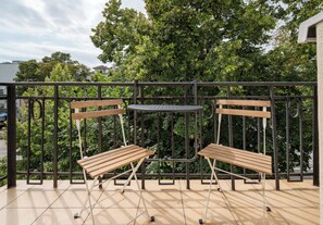 Ein Balkon mit Metallgeländer, zwei Holzbanken und einem kleinen runden Tisch.