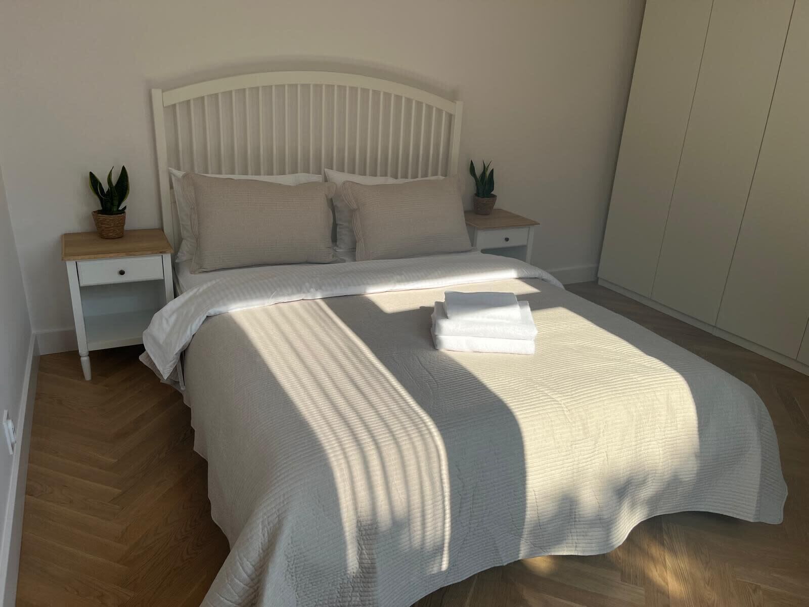 A neatly made bed with a white headboard and two bedside tables, each with a plant.