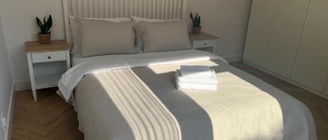 Una cama bien hecha con un cabecero blanco y dos mesitas de noche, cada una con una planta.