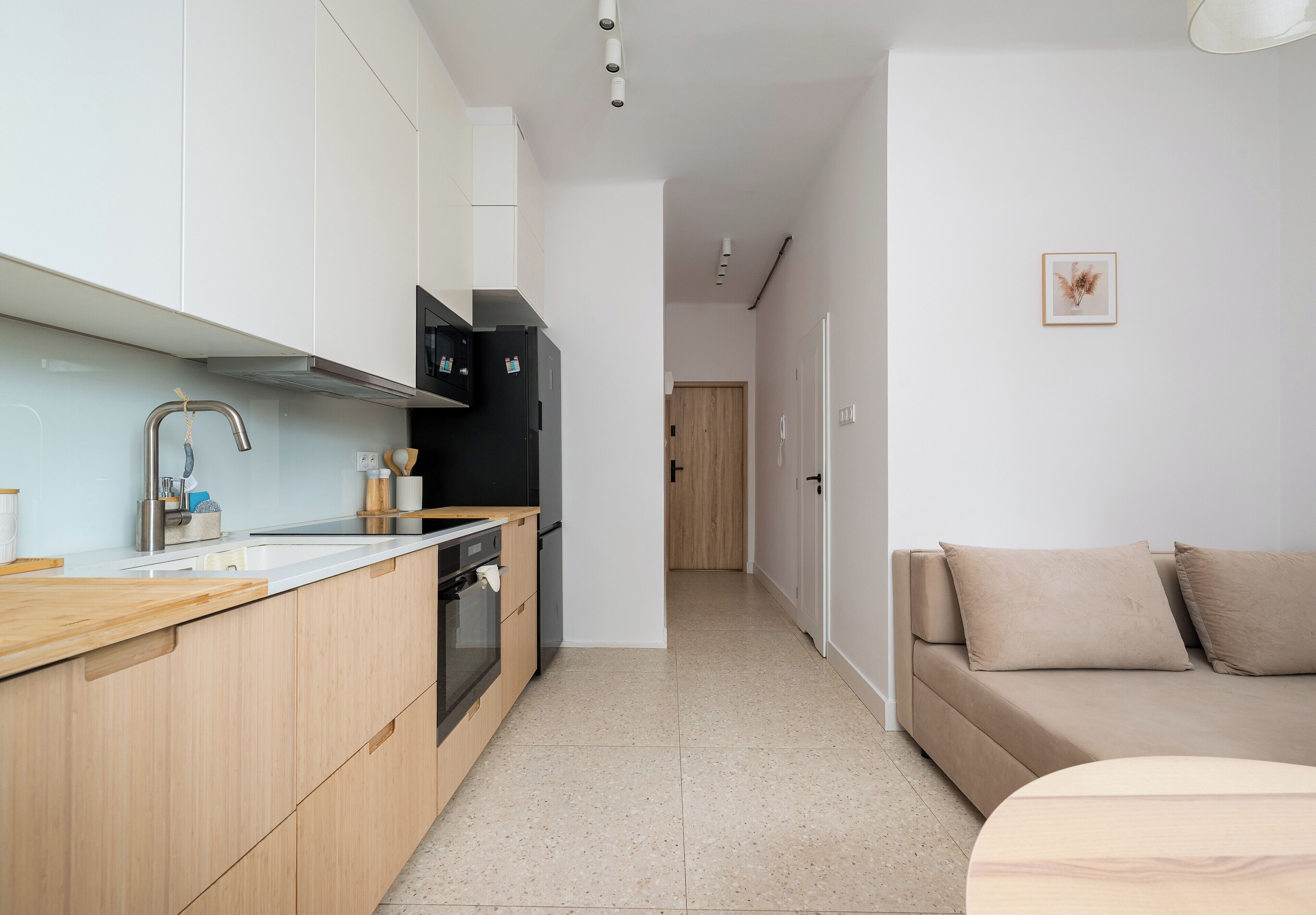 Una cocina moderna con encimera de madera, electrodomésticos de acero inoxidable y vistas a una sala de estar con un sofá y un cuadro en la pared.