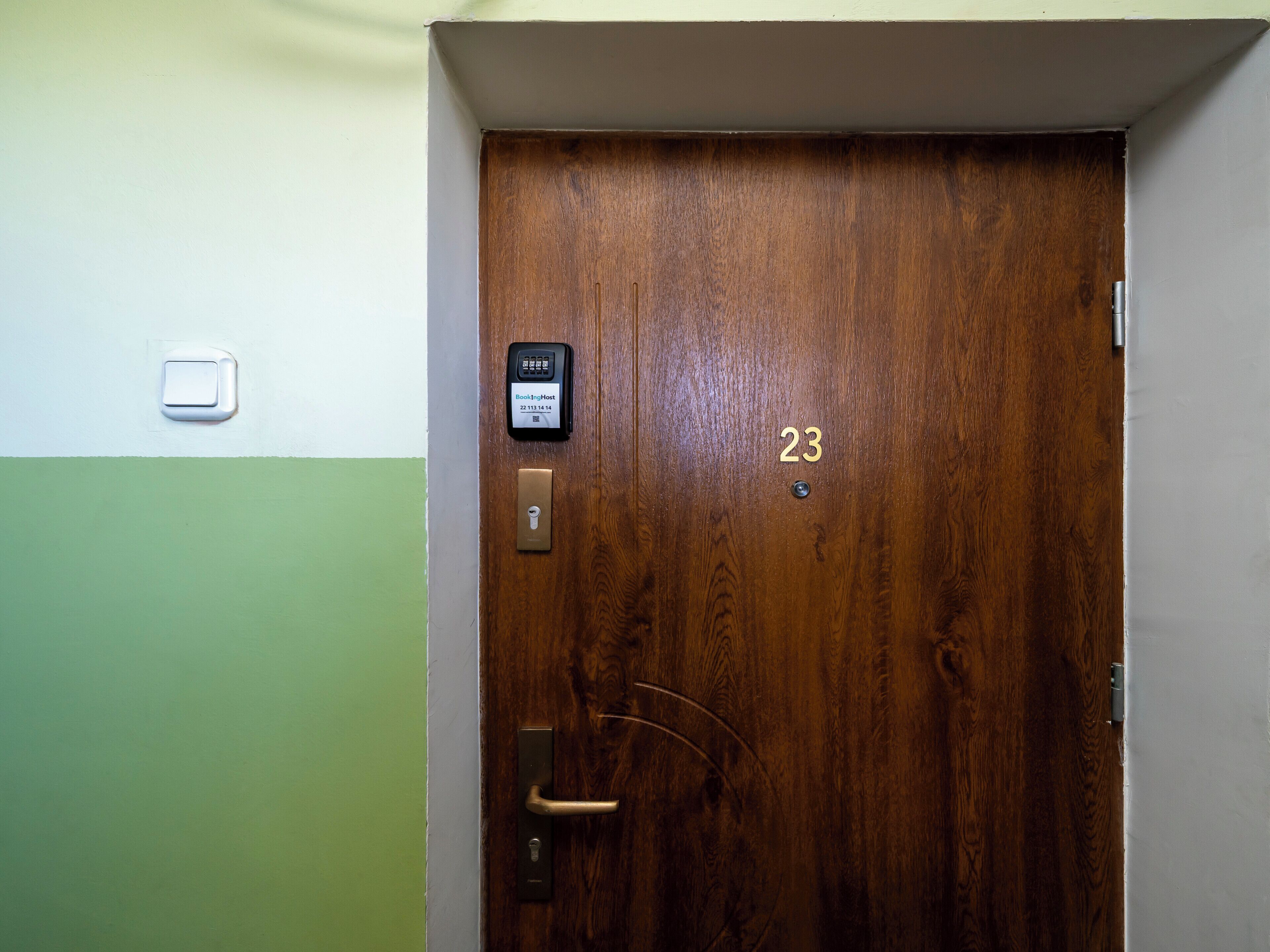 Uma porta de madeira com teclado numérico e fechadura, e um interruptor de luz pequeno na parede.