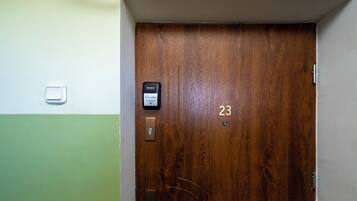 Uma porta de madeira com teclado numérico e fechadura, e um interruptor de luz pequeno na parede.