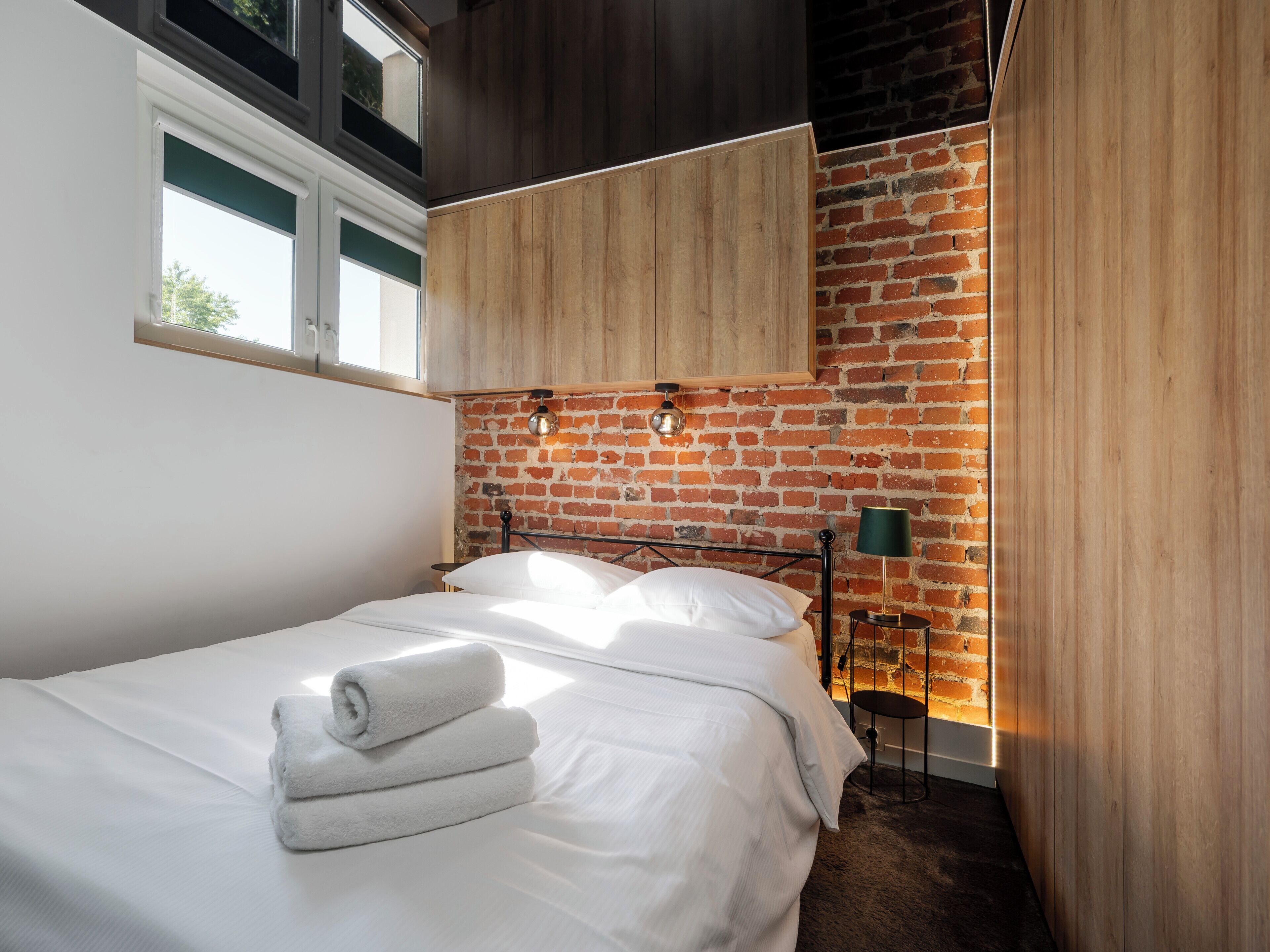 A hotel room with a bed, a brick wall, and a window.
