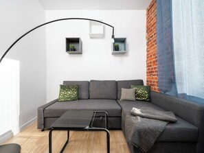 Ein modernes Wohnzimmer mit einem grauen Ecksofa, einem schwarzen Couchtisch und zwei an der Wand befestigten Regalen mit Pflanzen.