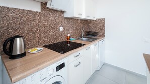 Ett modernt kök med en inbyggd tvättmaskin, en vattenkokare i rostfritt stål och en diskho med en svart kran.