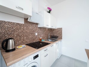 A modern kitchen with a built-in washing machine, a stainless steel kettle, and a sink with a black faucet. - Piotrkowska Elegant Studio (Łódź)