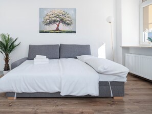 A bedroom with a bed, pillows, a bedside plant, and a painting of a tree. - Piotrkowska Elegant Studio (Łódź)