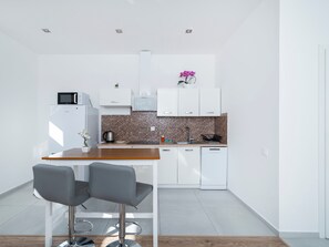 Cozinha moderna com armários brancos, bancada de madeira e um banco alto.