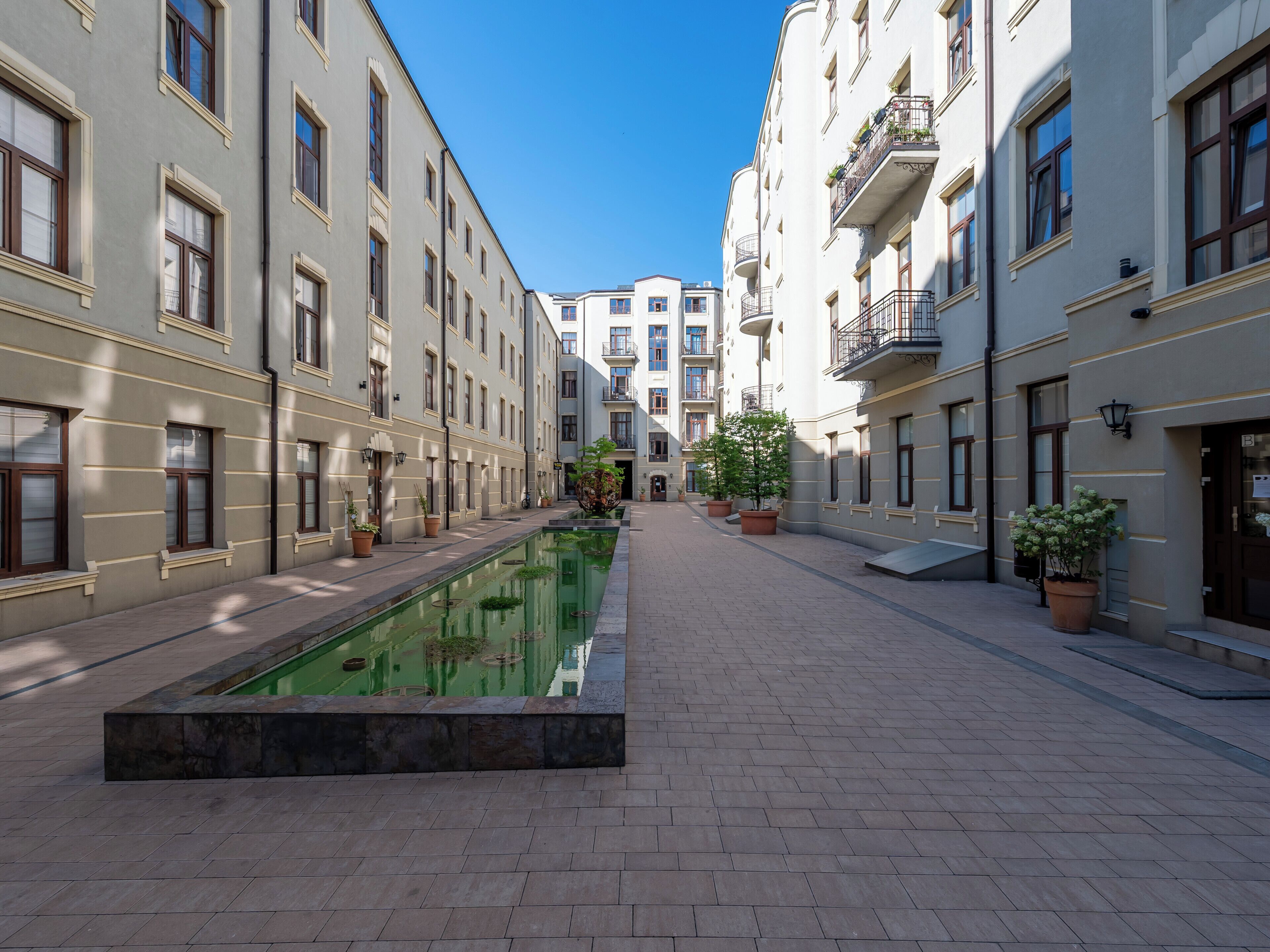 A courtyard with a rectangular pool, potted plants, and multi-story buildings with balconies.