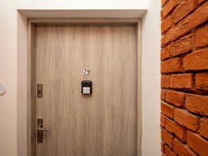 A wooden door with a numeric keypad and a lock, adjacent to a brick wall. - Piotrkowska Elegant Studio (Łódź)