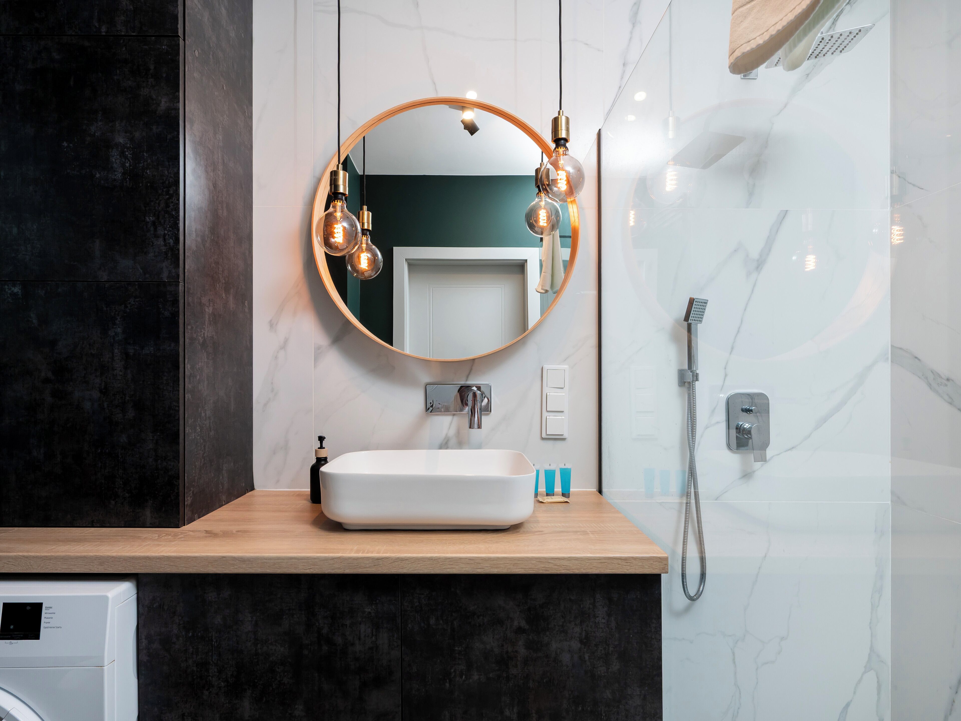 A modern bathroom with a round mirror, a white sink, and a shower.