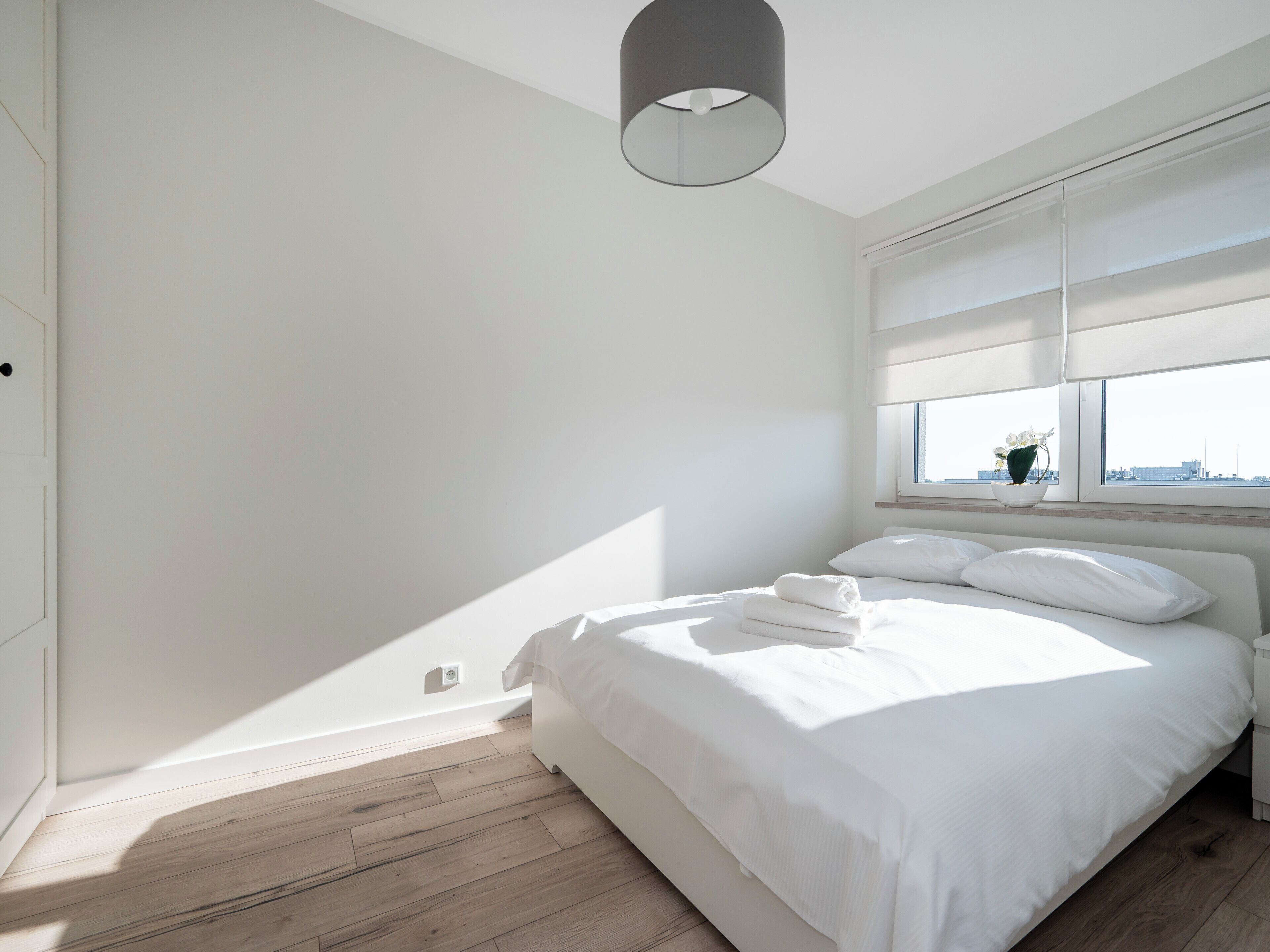 Ein schlicht eingerichtetes Schlafzimmer mit einem großen Bett, einem Fenster mit Ausblick und einer Deckenleuchte.