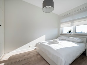 Ein schlicht eingerichtetes Schlafzimmer mit einem großen Bett, einem Fenster mit Ausblick und einer Deckenleuchte.