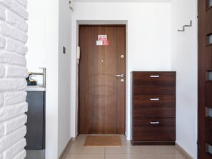 A wooden door with a doormat, a small cabinet with drawers, and a white brick wall. - 1 Maja Homely Apartament (Łódź)
